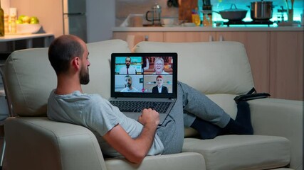 Poster - Comfortable man relaxing on couch while having online business conference with collegues using laptop computer during quarantine. Focused adult talking on videocall use webcam late at night in kitchen