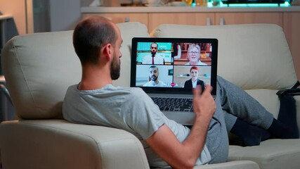 Poster - Tired man sitting comfortable on sofa while chatting with teammates about social communication during business videocall conference using laptop computer late at night in kitchen