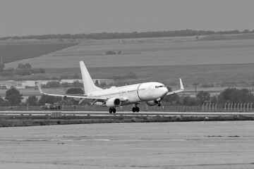 Wall Mural - Side view of white commercial passenger jet airliner in flight landing on airport runway. Black and white widescreen frame. Modern technology in fast transportation, business travel aviation, tourism.