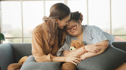 Mother supporting sweet down syndrome daughter to learn and relax from the internet, embracing child to encourage down syndrome girl at home.