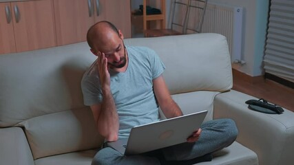 Poster - Tired man sitting on sofa while talking with collegue during business videocall conference using laptop computer, Caucasian male working from home because of coronavirus quarantine late at night