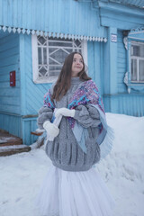 Wall Mural - Russian girl in vintage Pavlovo Posad shawl  (Pavlovoposadsky shawl) and blue rural wooden house with carved windows in Russian village. Russian folk style in architecture and architectural fashion