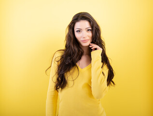 Charming young brunette woman with perfect brown curlyg hair and positive face expression posing at studio over yellow background.