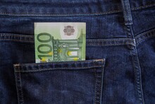 One Hundred Dollar Note In The Back Pocket Of Blue Jeans. Dollars Bills In Jeans Pocket Close-up.