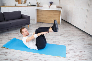 Wall Mural - A strong athletic man in a T-shirt and doing press exercises at home in his spacious and bright apartment with a minimalistic interior. Doing sports at home.