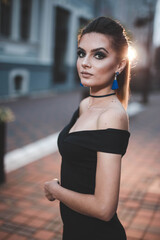 Sticker - Vertical shot of an attractive young female in an elegant black dress posing in the street at night