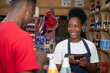 © Confidence - african shop attendant attending to a customer in a supermarket, accepting mobile funds transfer as payment