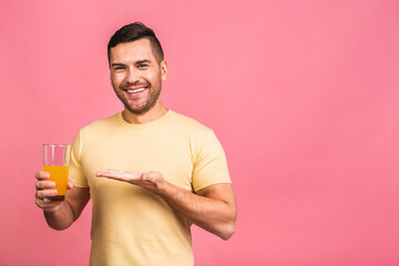 So tasty and healthy diet concept. Attractive young man holding a glass with orange detox juice drink, isolated over pink background, copy space.