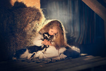 Beautiful Little Girl With Long Hair With A Little Lamb In The Hayloft In Russia. Image With Selective Focus And Toning