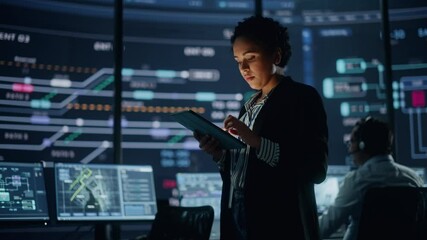 Aufkleber - Young Multiethnic Female Government Employee Uses Tablet Computer in System Control Monitoring Center. In the Background Her Coworkers at Their Workspaces with Many Displays Showing Technical Data.