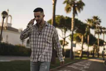 Poster - Handsome European man in a plaid shirt walking outdoors and talking on the phone