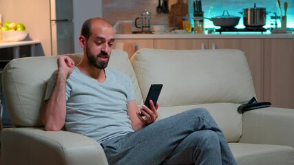 Poster - Caucasian male talking with his collegue about business conference using phone while standing in pajamas on couch. Tired man working late at night in kitchen using modern technology wireless