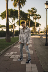 Wall Mural - Vertical shot of a stylish European man in a plaid shirt standing outside against palm tree