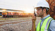 Railway engineer talking on a walkie-talkie at the train track.