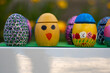 Hand-made Easter eggs on a green pedastal in front of yellow and orange spring flowers