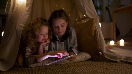 Wall Mural - Sisters indoors at home, using tablet in pajamas. Lockdown concept.