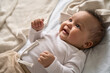 Happy healthy playful little cute adorable baby girl lying on comfortable bed or crib soft sheet. Smiling small sweet funny mixed race infant child laughing at home. Close up view