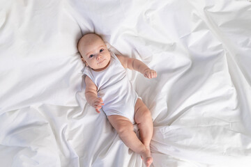 Wall Mural - baby on the white bed on the bed in the morning. Textiles and bed linen for children. A newborn baby has woken up or is going to bed