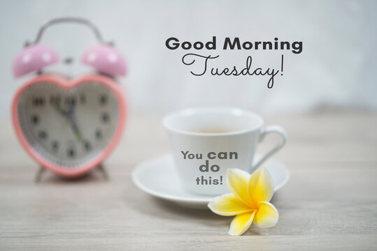Wall Mural -  - Good morning Tuesday. You can do this. Tuesday concept with morning inspirational quote on cup of morning coffee, pink alarm table clock and yellow Bali frangipani flower on white table background.