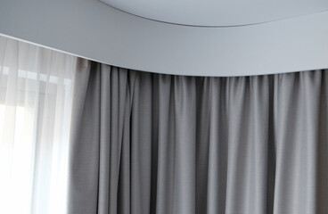 Angular cornice with drapes and white curtain or tulle. Interior details close up. White wall, ceiling, cornice niche, curtains on the window. Corner white plastic hidden curtain rod.