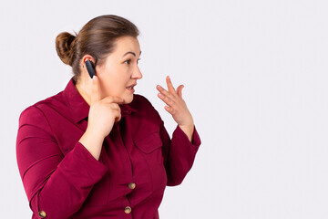 Young plus size, business woman talking, making call via wireless earphones, looking side to empty blank space. Hands free device at workplace.