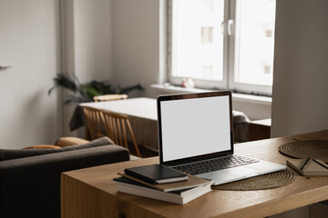 Laptop with blank copy space screen on table with notebooks on wooden table. Minimalist home office workspace. Mockup template.