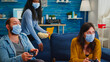 © DC Studio - Excited group of multiethnic friends celebrating victory while playing video games in living room keeping social distancing wearing face mask during global pandemic. People enjoying time together.