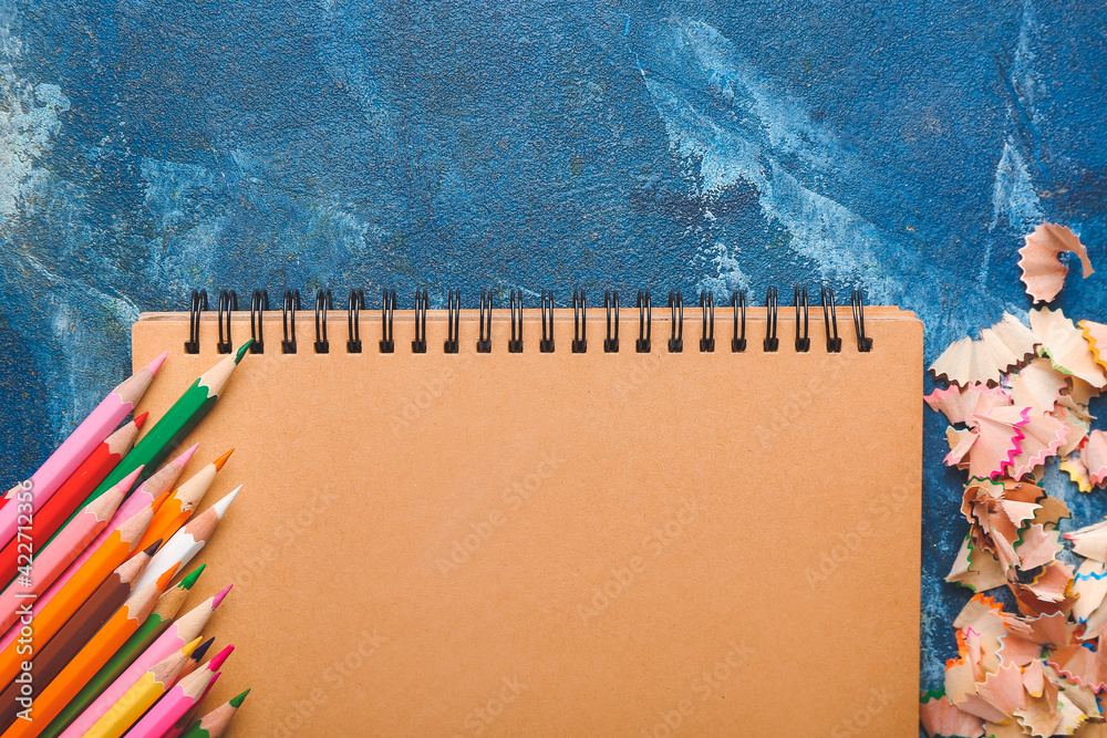 Notebook, pencils and shavings on color background