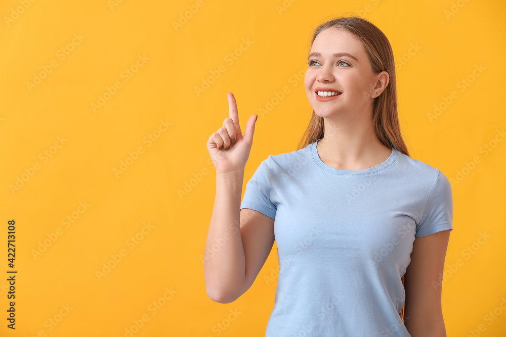 Beautiful smiling young woman pointing at something on color background