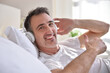 © Davizro Photography - Smiling man listening music lying in bed ok sign