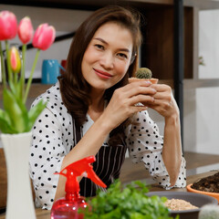 Wall Mural - Beautiful Asian woman wearing apron showing a small pod of cactus with happy and proud for her hobby and home gardening in free time