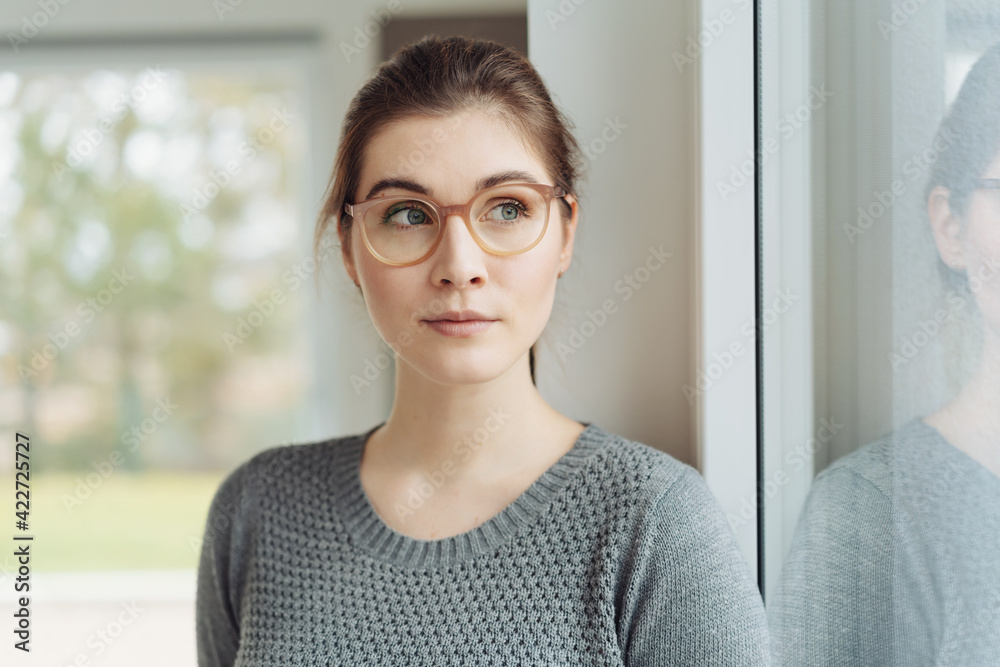 Attractive young woman wearing eyeglasses looking aside through a window - obrazy, fototapety, plakaty 
