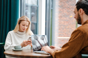 Sticker - Focused man and woman using laptop and cellphone while drinking coffee