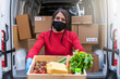 Portrait of a young female courier holding a basket of food about to be delivered to customer bought at supermarket - Millennials wearing face mask and gloves during global pandemic from Coronavirus