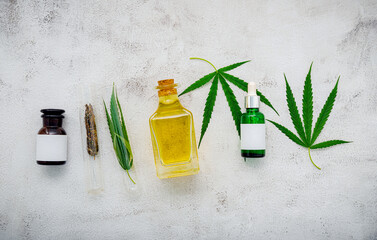 Wall Mural - Glass bottle of cannabis oil and hemp leaves set up  on concrete background.