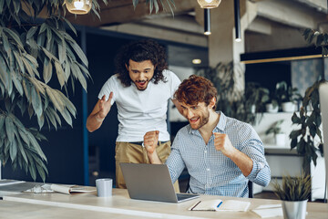 Two excited overjoyed young businessmen looking at laptop screen happy to win or recieved good news