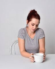 Poster - 3/4 close up portrait of red haired girl wearing striped shirt and drinking tea.  studio background.