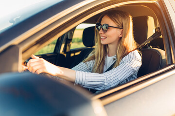 Wall Mural - young happy smiling woman driving her new car at sunset