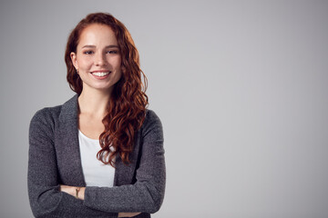 Wall Mural - Studio Portrait Of Smiling Young Businesswoman With Folded Arms Against Plain Background