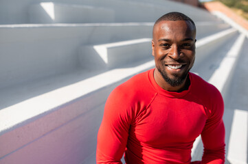 Portrait of smiling black sportsman sitting on stairs.