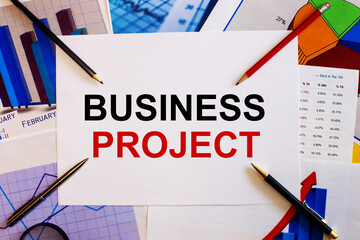 Fototapete - The words BUSINESS PROJECT is written on a white background near colored graphs, pens and pencils. Business concept