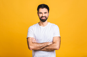 Wall Mural - Happy young man. Portrait of handsome young man in casual keeping arms crossed and smiling while standing isolated over yellow background.