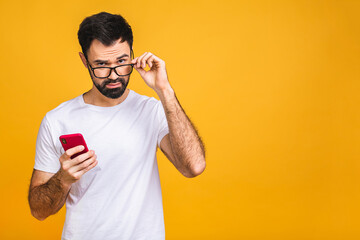 Wall Mural - Always in touch. Happy young amazed shocked bearded man in glasses typing sms on yellow background.