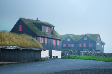 Wall Mural - Foggy morning view of a house with typical turf-top grass roof and blue cloudy sky in the Velbastadur village on Streymoy island, Faroe islands, Denmark. Landscape photography