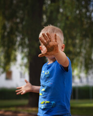 little boy  shows his dirty palm in the sand and covers his face