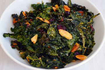 Bowl of cooked green kale salad with dried cranberries and almonds