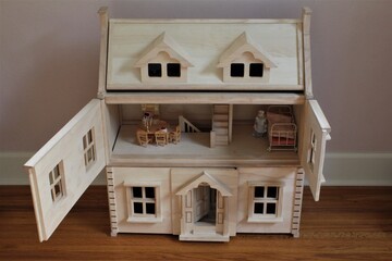 A DIY wooden doll house in a child's room to play pretend. The doors are open on the second floor and the dolls room is shown with miniature furniture. 