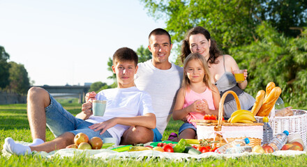 Wall Mural - Happy parents with two kids having picnic together on green meadow in park. High quality photo