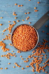 Wall Mural - Red lentils in a metal measuring cup on a blue natural wood background. Top view.