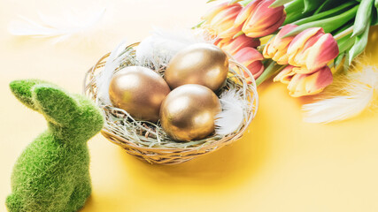 Wall Mural - Easter Golden colour eggs in basket with spring tulips, white feathers on pastel yellow background in Happy Easter decoration. Festive decoration.